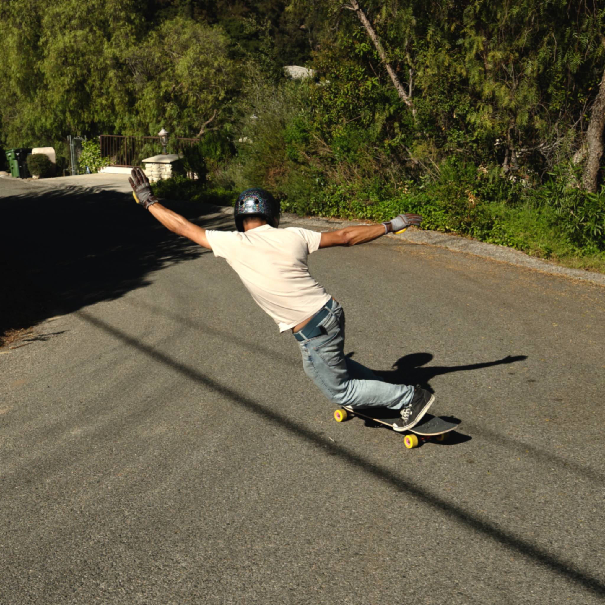 Skater in a helmet doing a standup slide on a sunny residential street on yellow Orangatang Beefcake 73mm wheels