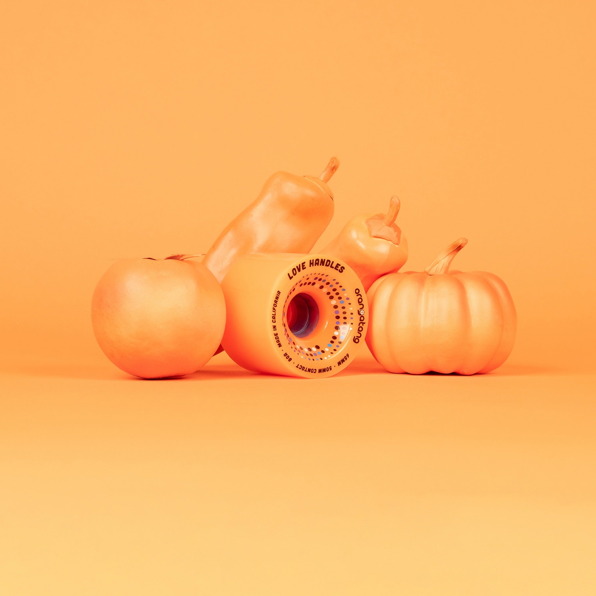 Orange Orangatang Love Handles 65mm wheel arranged with orange-painted pumpkins and gourds on an orange background