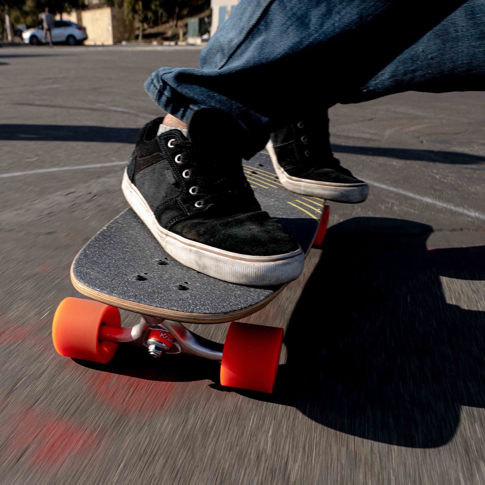 Close-up of a skater's black sneakers on a cruiser board rolling on orange Orangatang Love Handles 65mm wheels