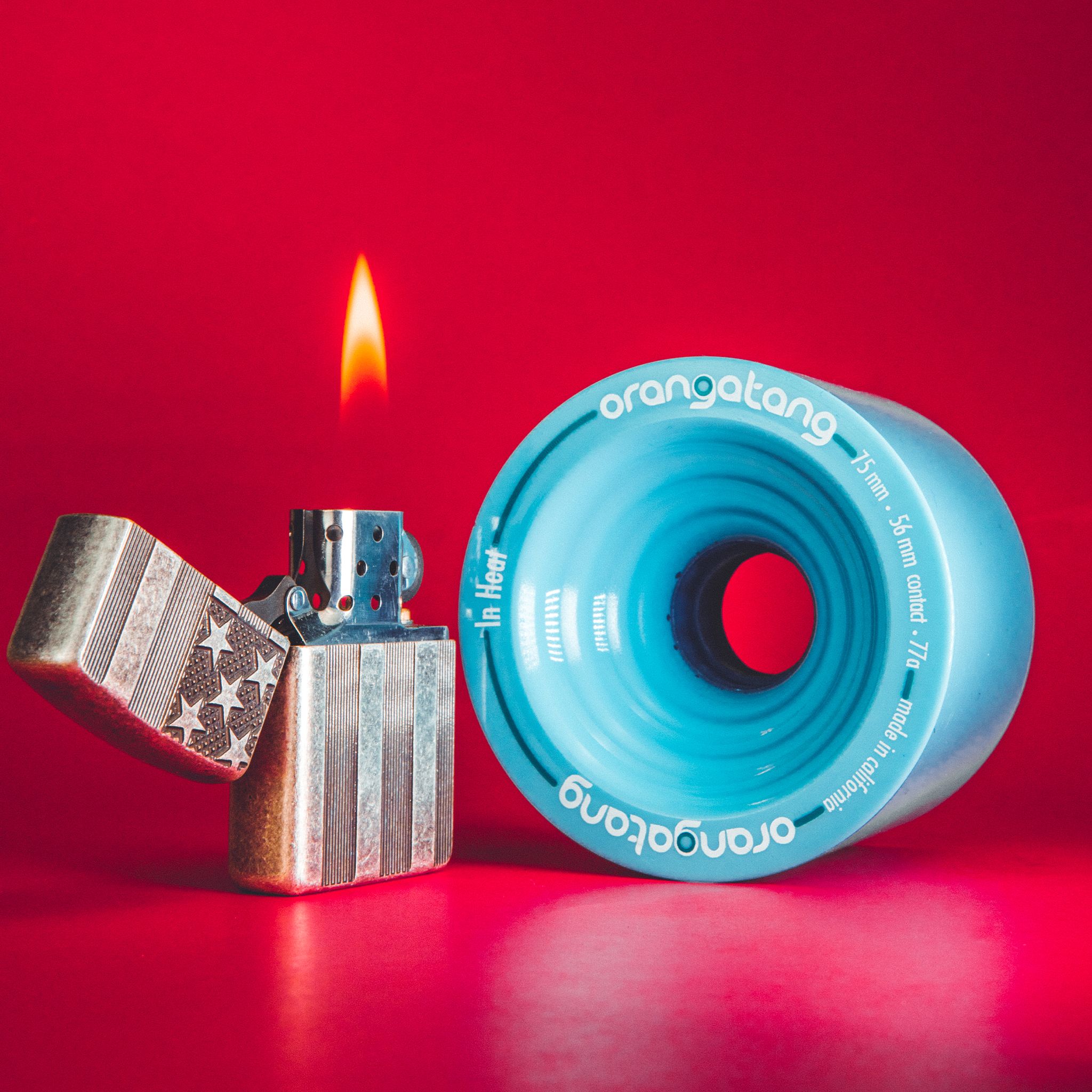 Light blue Orangatang In Heat 75mm wheel next to a lit flip-top lighter on a red background