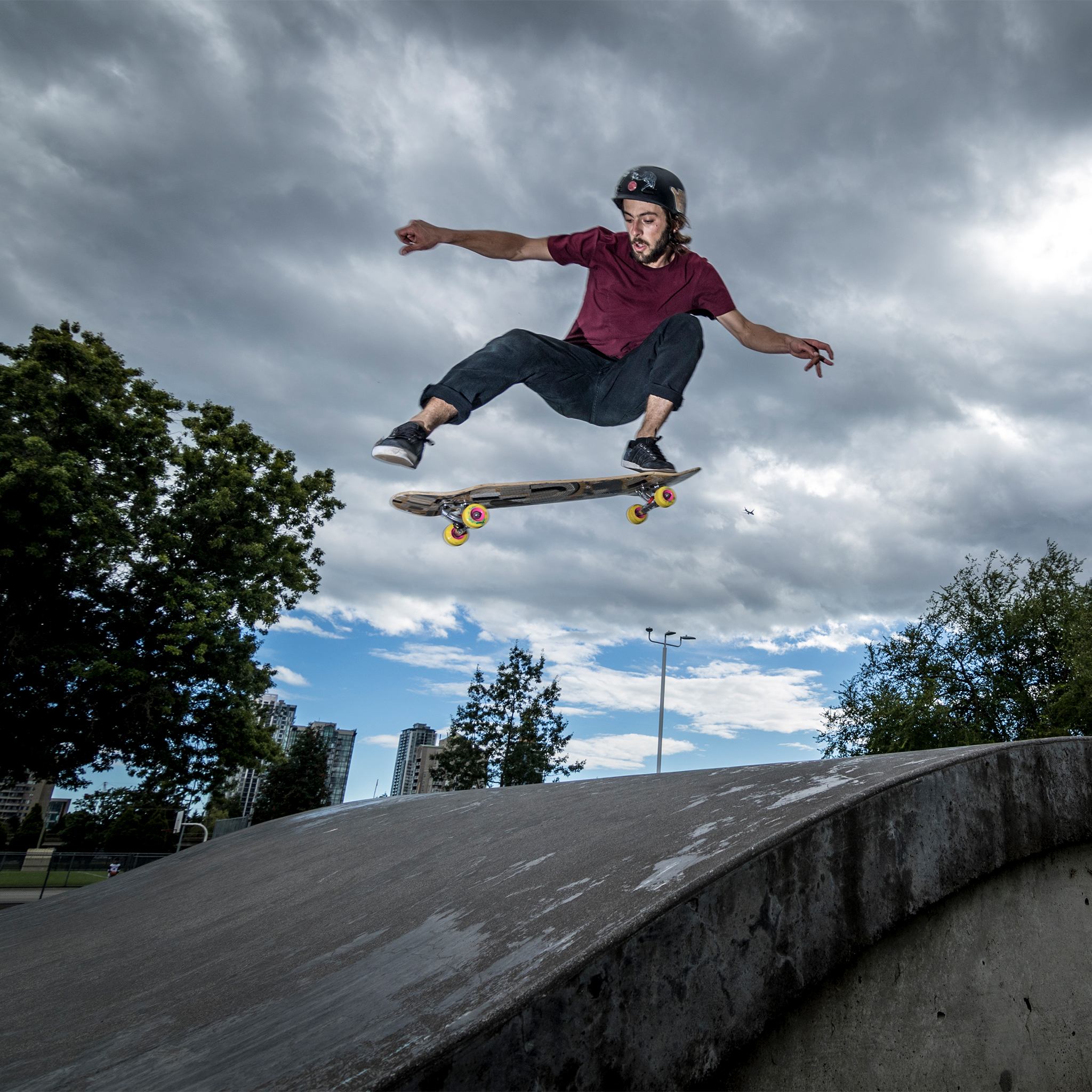 Skater in a helmet airing out of a concrete bowl on a board with yellow Orangatang Skiff 62mm wheels under a cloudy sky