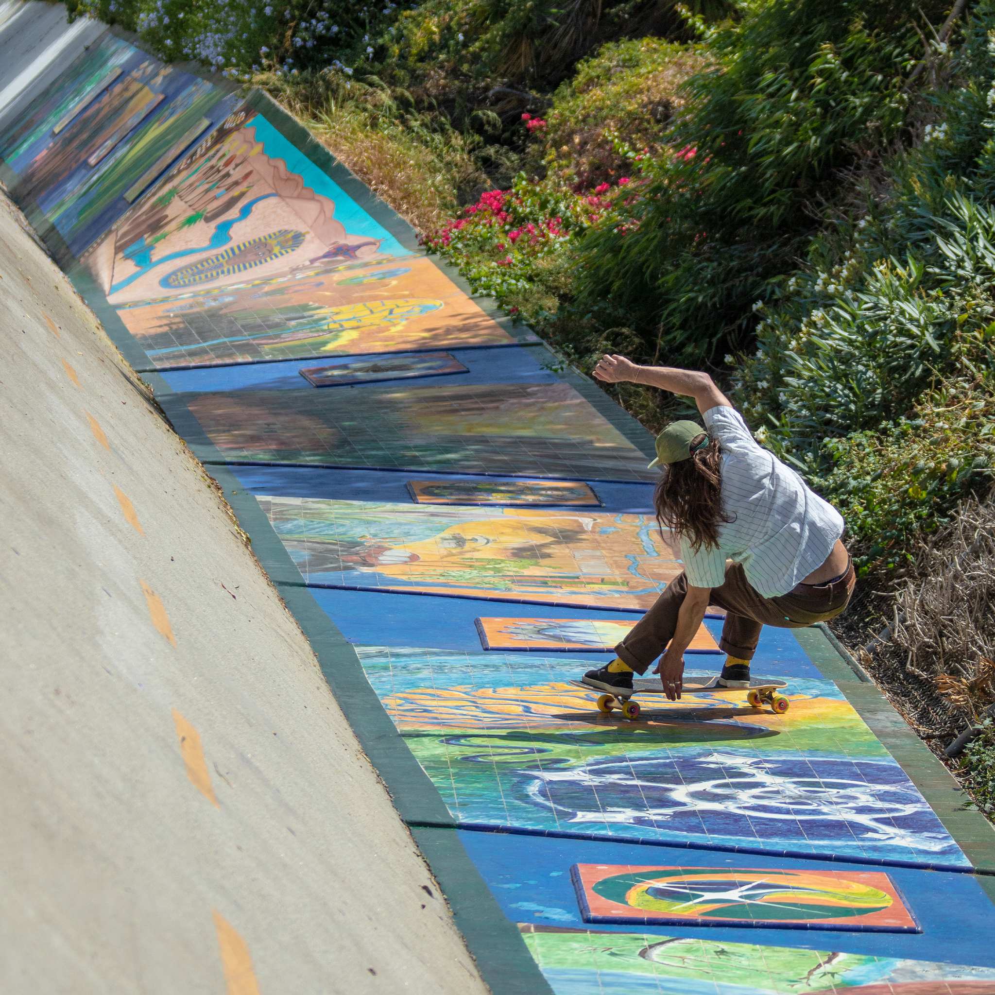 Skater carving down a mural-painted concrete bank on a cruiser board with yellow Orangatang Skiff 62mm wheels