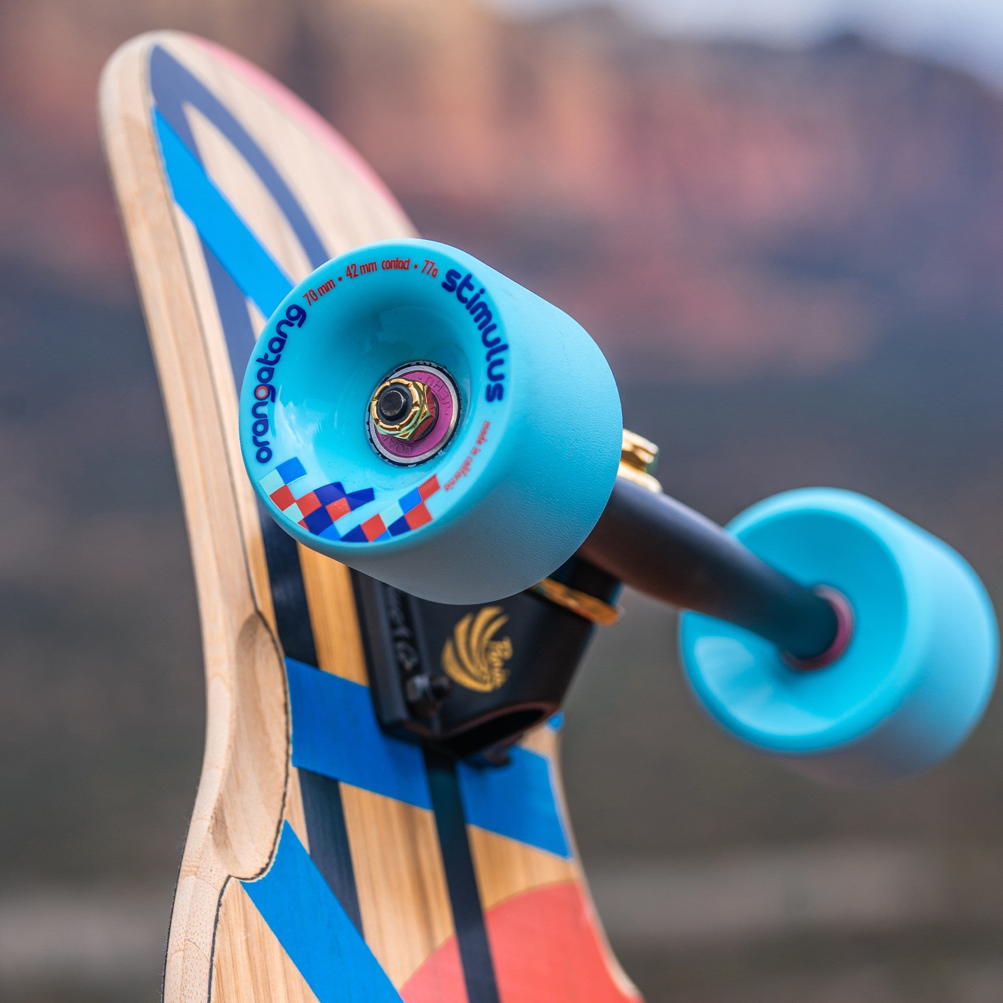 Light blue Orangatang Stimulus 70mm wheel mounted on a longboard truck, held up against a canyon landscape