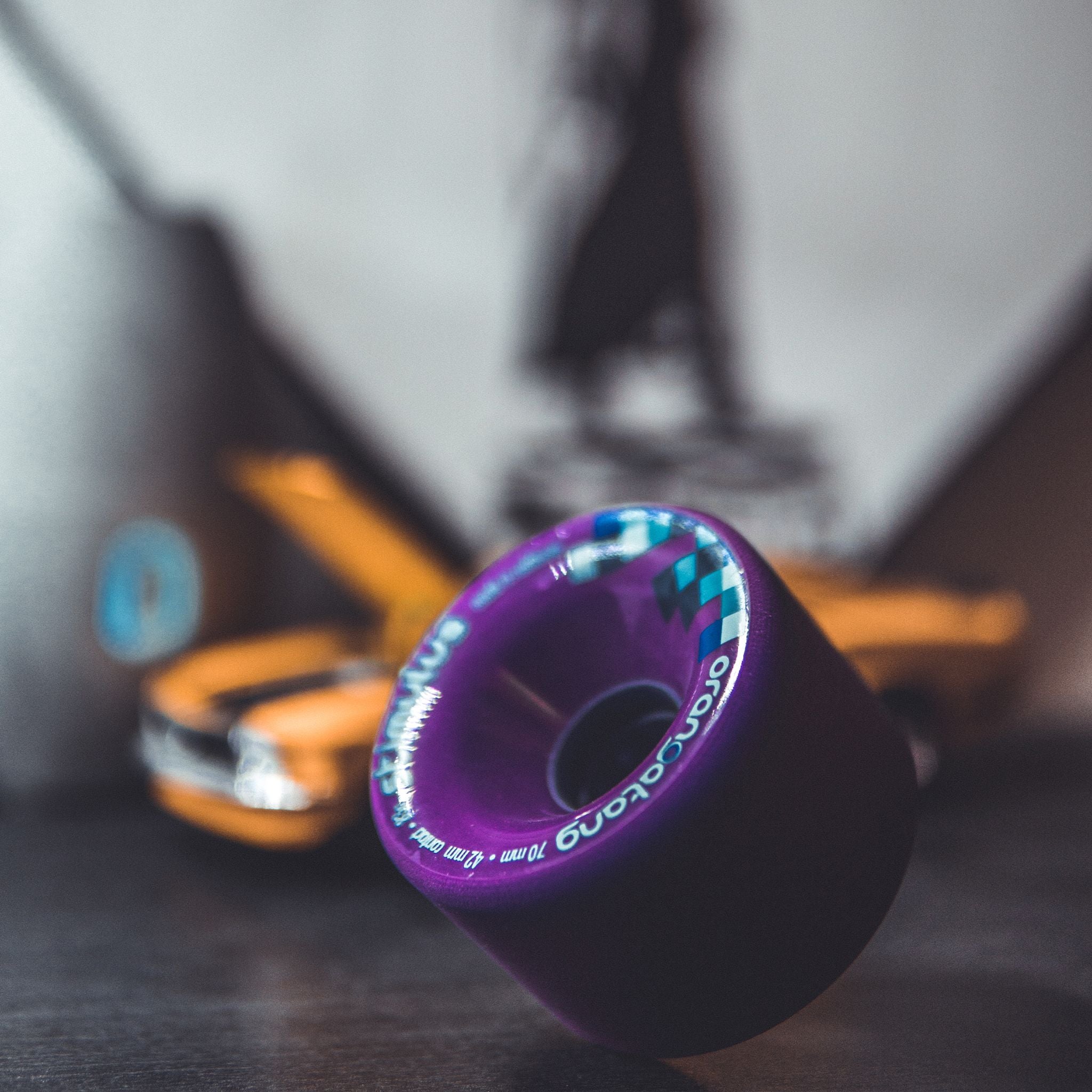 Purple Orangatang Stimulus 70mm wheel standing on a table with a blurred toy orange muscle car behind it